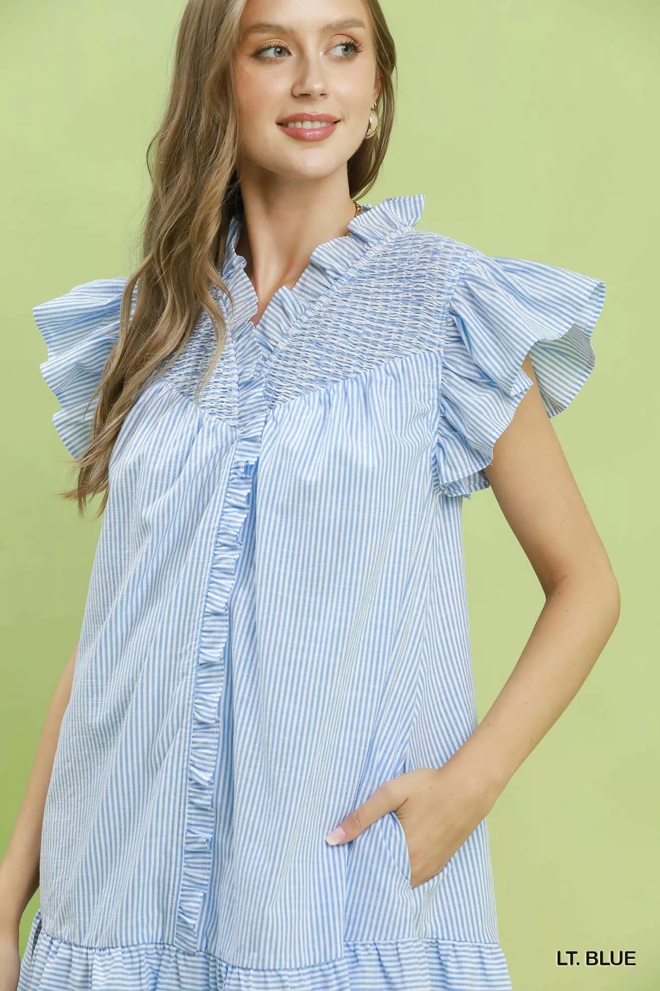 Woman wearing a light blue and white striped dress with ruffled sleeves against a green background