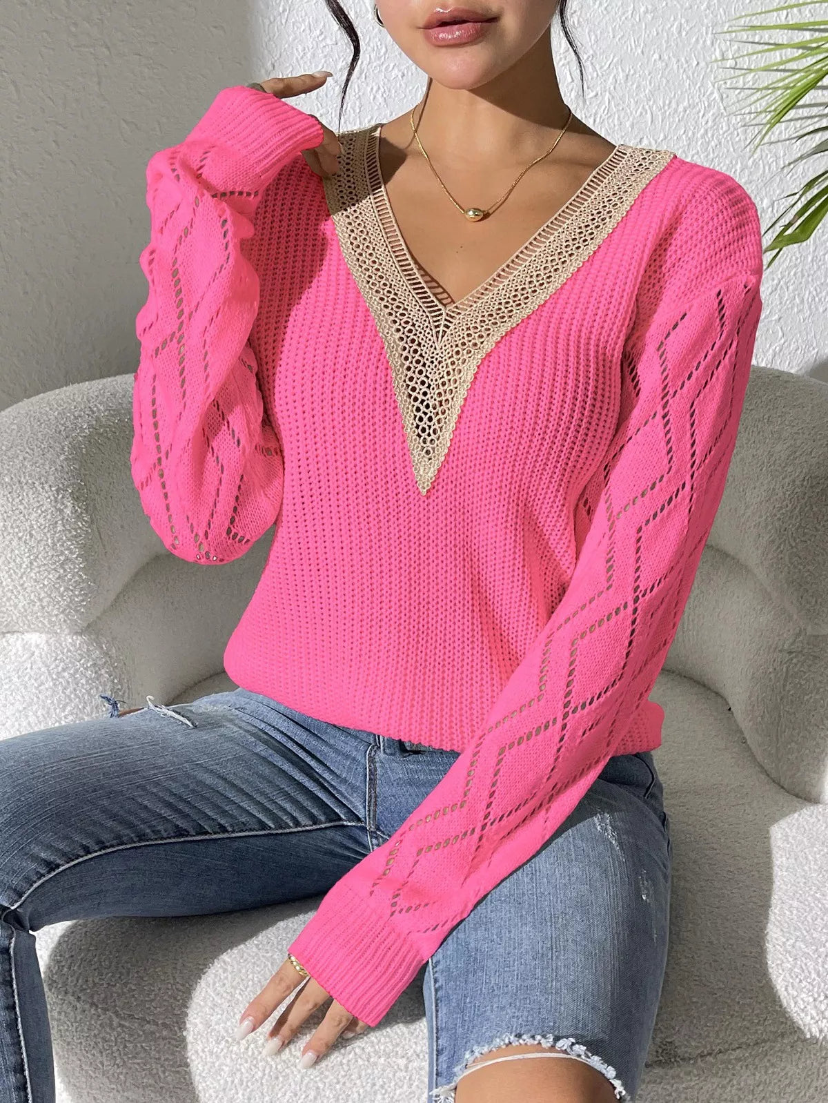 Woman wearing a fuchsia pink V-neck hollow knit sweater with contrasting neckline, openwork long sleeves, and blue jeans.