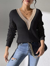 Woman wearing a black V-neck hollow knit sweater with contrasting neckline, openwork long sleeves, and blue jeans.