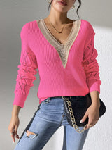 Woman wearing a fuchsia pink V-neck hollow knit sweater with contrasting neckline, openwork long sleeves, and blue jeans.