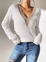 Woman wearing a gray/white V-neck hollow knit sweater with contrasting neckline, openwork long sleeves, and blue jeans.