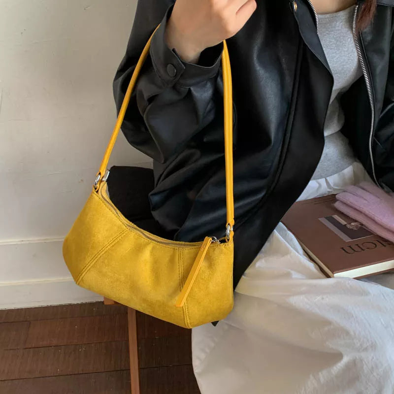 Yellow suede vintage-style shoulder bag with a minimalist silhouette paired with a neutral outfit.