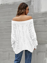 Woman wearing a white cable knit openwork off-shoulder sweater with distressed jeans and a wide-brim hat.