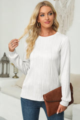Woman wearing a white textured round neck long sleeve blouse with dark-wash jeans, tan belt and brown clutch.
