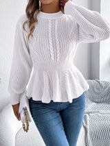 Woman wearing a white cable knit round neck peplum sweater with long sleeves and blue jeans.