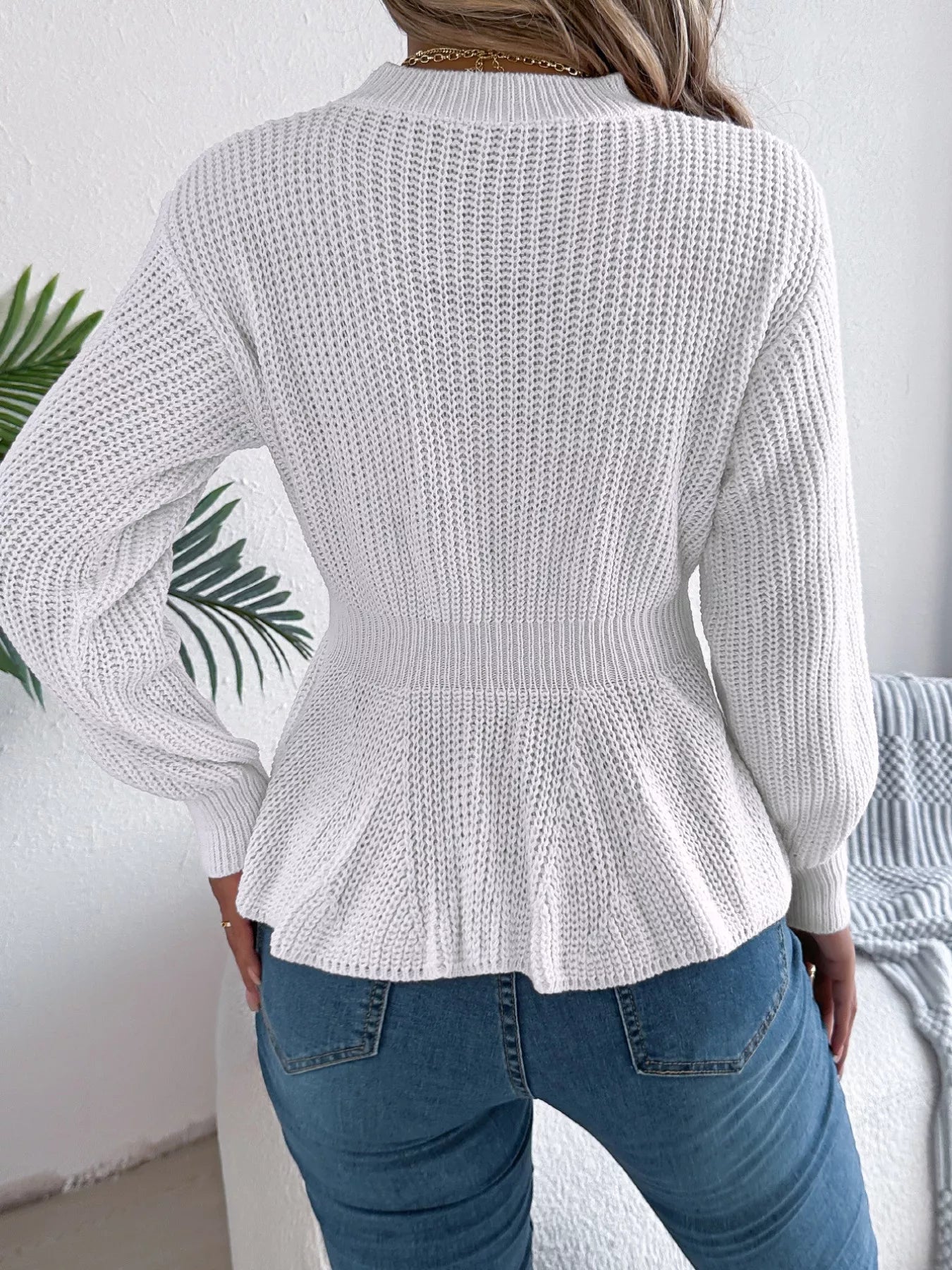Woman wearing a white cable knit round neck peplum sweater with long sleeves and blue jeans.