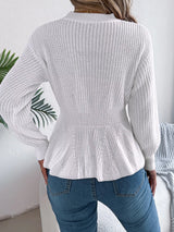 Woman wearing a white cable knit round neck peplum sweater with long sleeves and blue jeans.