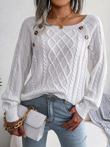Woman wearing a white cable-knit sweater with decorative buttons, paired with light-wash jeans, layered gold necklaces, and a white handbag. Perfect for cozy fall and winter outfits.