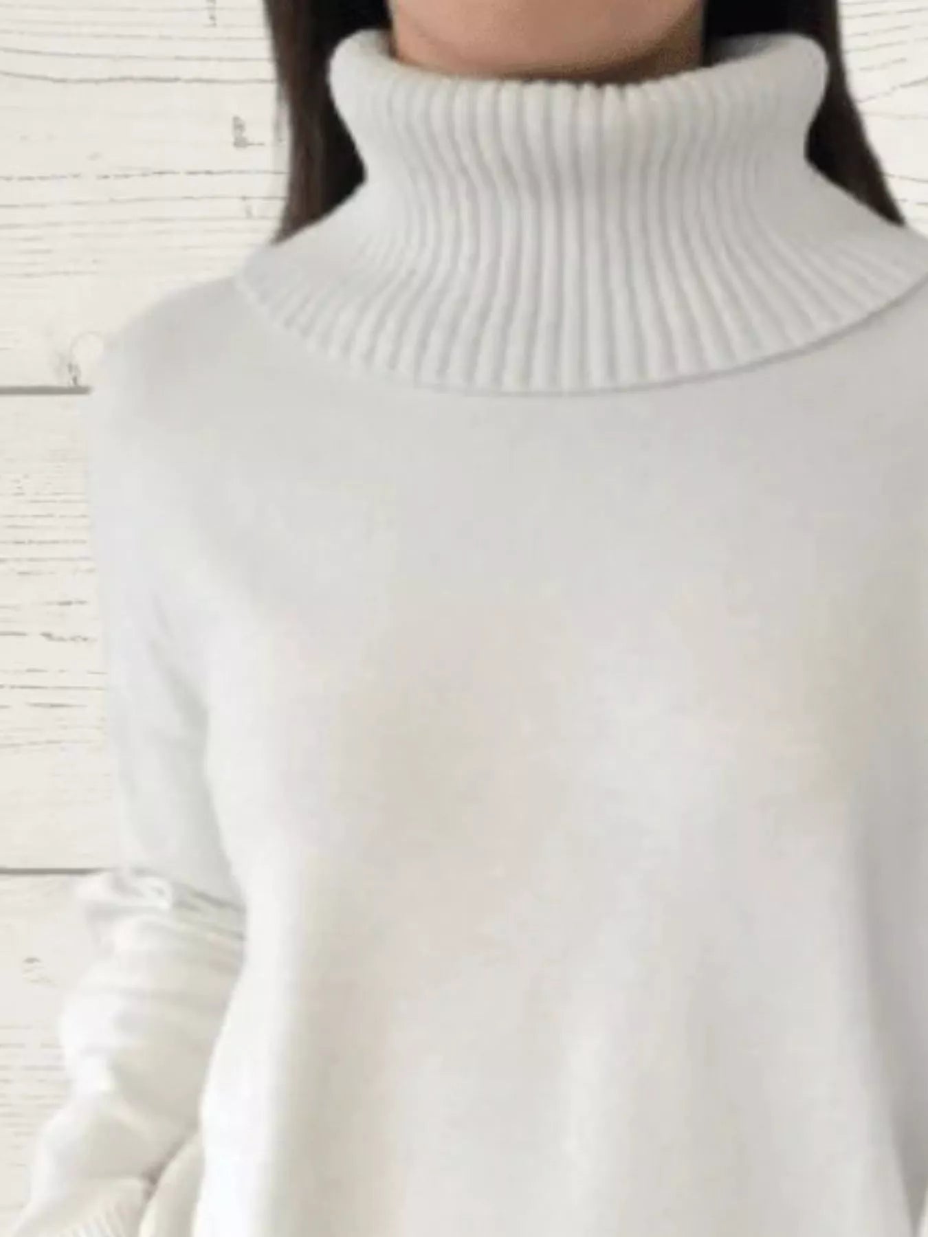 Woman wearing a white ribbed turtleneck sweater with decorative button sleeves and jeans.