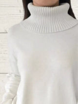 Woman wearing a white ribbed turtleneck sweater with decorative button sleeves and jeans.