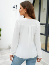 Woman wearing a white notched neck long sleeve blouse with flounce cuffs styled with light-wash jeans.