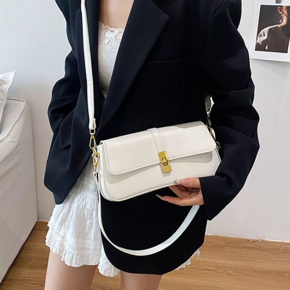 White rectangular crossbody handbag with a gold turn-lock buckle and adjustable shoulder strap displayed on a modern tabletop.