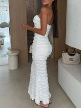 Woman wearing a white sweetheart neck tube maxi dress with ruched detailing and a subtle cutout, styled with an ivory clutch for an elegant evening look.