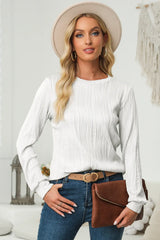 Woman wearing an white textured round neck long sleeve blouse with dark-wash jeans, tan belt, brown clutch and cream hat.