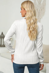 Woman wearing a white textured round neck long sleeve blouse with dark-wash jeans.