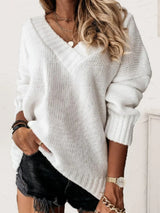 Woman wearing a white V-neck long sleeve knit top with ribbed neckline and cuffs, styled with black denim shorts.