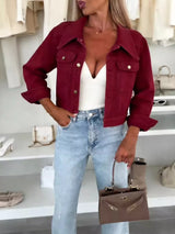 Woman wearing a wine red cropped denim jacket over a white top with light-wash jeans and a structured handbag, styled for a chic fall outfit.