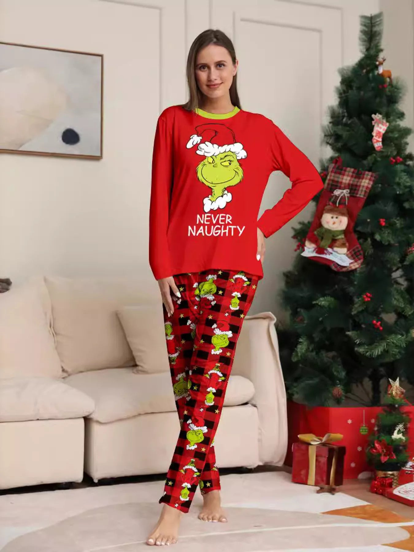 Woman modeling matching red Grinch-themed Christmas pajamas with festive graphic tops and red and black character-print pants.