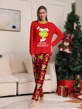 Woman modeling matching red Grinch-themed Christmas pajamas with festive graphic tops and red and black character-print pants.