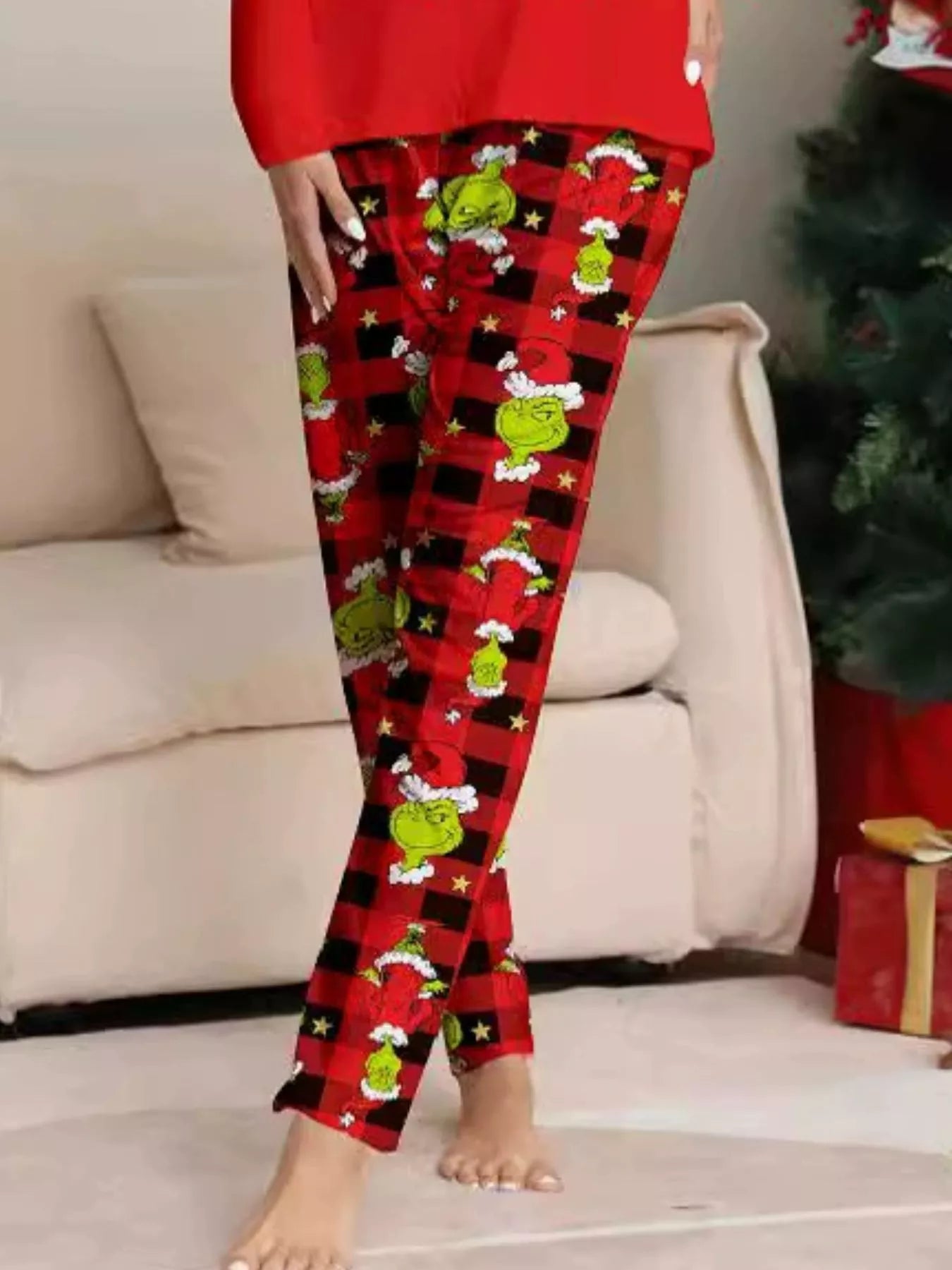 Woman modeling matching red Grinch-themed Christmas pajamas with festive graphic tops and red and black character-print pants.