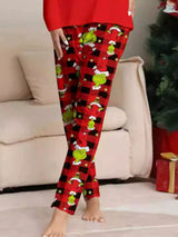 Woman modeling matching red Grinch-themed Christmas pajamas with festive graphic tops and red and black character-print pants.